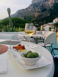 olives and wine it on a white table overlooking verdant cliffs