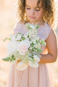 flower girl looking down at bouquet of flowers