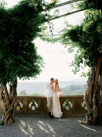 A couple leaning against an ornate stone balcony, illustrating the refined composition and heirloom quality of an estate wedding weekend.