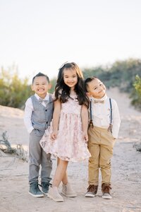 Three children from the Collins family smiling together in the Las Vegas desert, dressed in coordinated outfits during a joyful golden hour outdoor family photography session.