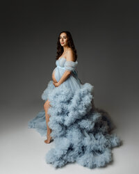 Expecting mom standing in a flowing blue maternity dress with a dramatic train, showcasing her pregnancy in the Inland Empire by Kaitlyn Dawn Photography.