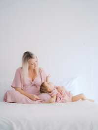 Mom and toddler daughter are laying on a bed in a studio maternity session in Seattle