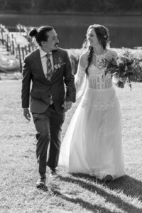 A wedding couple holding hands and walking through a vineyard