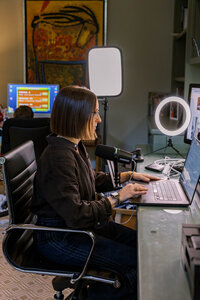 Leah Solivan sitting at her home office desk while her son plays a game behind her
