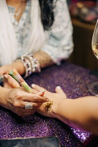 Applying a henna design on a hand over a sequined purple surface.