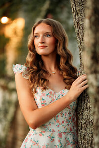 Senior portrait in downtown Magnolia Springs, Alabama — leaning against a tree in her flowery dress.