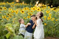 Jacksonville, FL portrait session capturing three siblings bursting into laughter while playing together in a sunflower field during an outdoor family session in Callahan.
