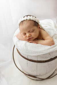 Newborn baby girl safely posed in a white wooden bucket at Jennifer Brandes Photography near Mankato, MN.