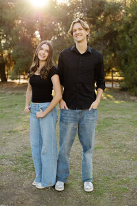 Siblings standing together in a sunlit park with coordinated black tops and jeans, modern outdoor portrait by Kaitlyn Dawn Photography, family and senior photographer.