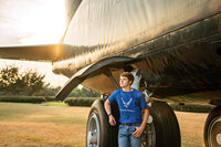 Senior portrait at Battleship Memorial Park in Mobile, Alabama— leaning against the tires of a c-130 looking off in the distance.