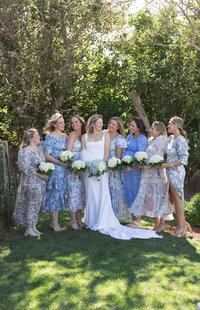 Bride poses with bridesmaids with floral dresses and hydrangea bouquets.