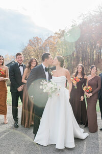 The newlyweds share a kiss outdoors, surrounded by their bridal party