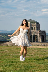 High school senior girl wearing a white dress and walking with the Columbia gorge in the background