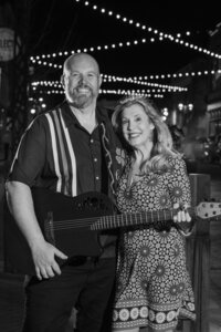 Black and white photo of two people smiling while one holds a guitar