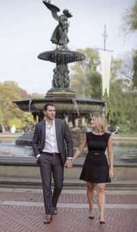 Central park engagement photos, Deborah Zoe Photography. A couple walk hand in hand in front of the Bethesda Fountain in Central Park.