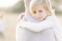 Close up photo of a boy hugging his dad and looking at his family photographer.