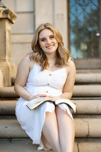 High school senior girl sitting on stone steps with a book in her lap, natural outdoor senior portrait by Kaitlyn Dawn Photography.