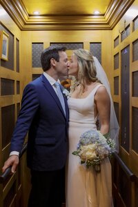 Bride and groom kiss in elevator lined with Louis Vuitton wallpaper.