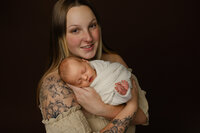 Mother smiling while holding her newborn during a studio session. Photographed by Inland Empire newborn photographer Kaitlyn Dawn Photography.