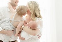 little boy kissing mom who is holding newborn