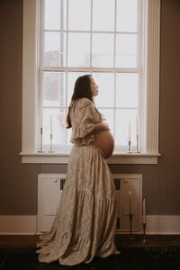 Woman standing in front of window at Maison Charlottesville during maternity Photoshoot