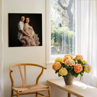 Framed maternity portrait displayed above a chair with flowers by a window in a light-filled home, Kaitlyn Dawn Photography, Yucaipa maternity photographer.