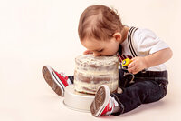 one year old taking first big bite of frosted birthday cake