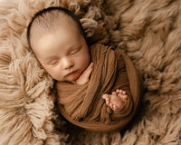 Sleeping newborn baby wrapped in a warm brown swaddle and posed on a textured blanket during a studio session with newborn photographer Kaitlyn Dawn Photography.