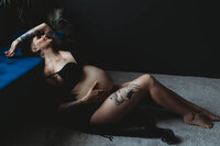 pregnant woman in lingerie leaning back against a couch with hand up