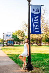 MTSU senior leaning against light post with the football stadium behind her