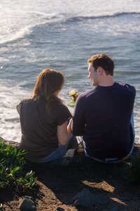 couple sitting on cliffside with ocean in santa cruz with flower