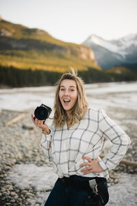 incredible calgary wedding photographer specializes in candid documentary style. Carly holding her camera, smiling. with her hair blowing in the mountains.