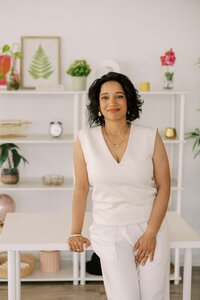Woman leaning casually on a table, wearing an all white outfit and smiling at the camera with a soft smile