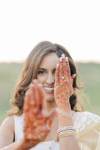 A woman showcasing her henna-adorned hands while smiling.