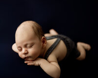 Sleeping newborn baby posed on tummy with a deep navy backdrop during a studio session with newborn photographer in Yucaipa at Kaitlyn Dawn Photography.