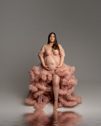 Expecting mother sitting in a blush ruffle maternity gown during an elegant studio maternity portrait session by Kaitlyn Dawn Photography.