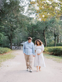 Expecting mom and her husband walking hand in hand in a path surrounded by trees in Seattle