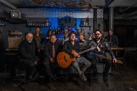 A band sitting and standing around a bar together