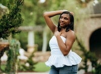 Senior portrait at Bella Sera Gardens in Loxley, Alabama — waist-up with hands near her waist
and greenery in the background.