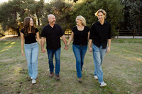 Family walking hand in hand through a grassy park during golden hour, candid lifestyle photography by Kaitlyn Dawn Photography, professional outdoor family portrait specialist.