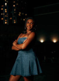 Senior portrait in downtown Mobile, Alabama — waist-up with arms crossed and bokeh city
lights in the background.