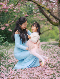 Expecting mom and toddler daughter laughing amongst falling cherry blossoms at UW Arboretum in Seattle