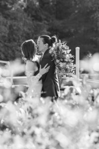 Black and white photo of a person kissing their partner in a field on their wedding day