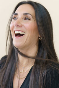 Young woman with long, dark hair laughing while taking a headshot photo