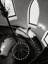 Dramatic high-angle editorial photograph of a bride descending the grand spiral staircase at Dover Hall Estate.
