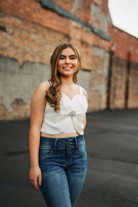 Senior portrait in downtown Mobile, Alabama — waist up smiling in front of a brick wall in a parking lot.