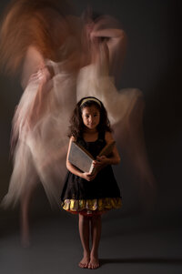 Girl in a black and gold dress standing still while blurred figures move around her in a long exposure.