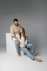 Father and mother seated on white studio cubes, modern neutral studio family portrait captured by Kaitlyn Dawn Photography.
