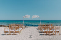 Cyprus Beach Wedding Ceremony overlooking the crystal blue sea set on white sand with blossom tree decoration and gold Chiavari chairs