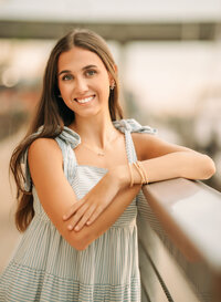 Senior portrait at The Wharf in Orange Beach, Alabama — leaning on a railing in a white-and-
blue striped dress, bridge behind her.